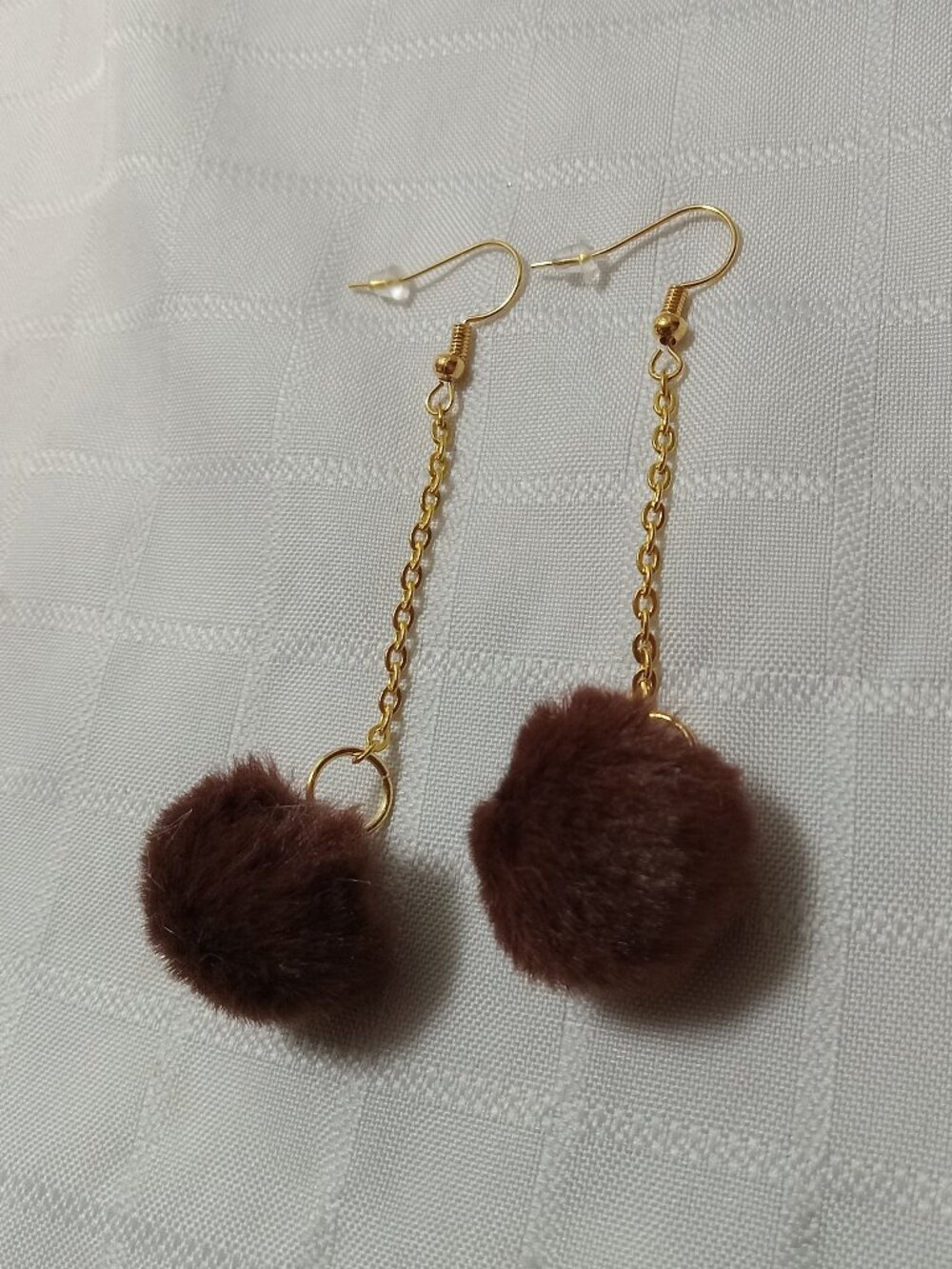 Handmade earrings with small pom-poms and gold-colored accent hooks and chains